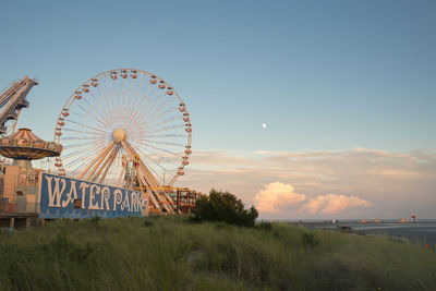 Ferris wheel at amusement park against sky during sunset