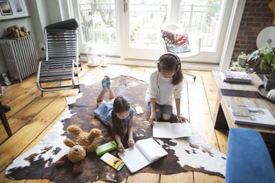 High angle view of sisters relaxing on carpet and studying at home