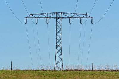 Low angle view of electricity pylon on field against clear sky