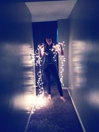 Portrait of young woman standing against illuminated wall