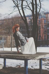 Woman standing by bare tree in winter