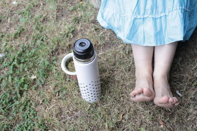 Low section of woman sitting by insulated drink container on field