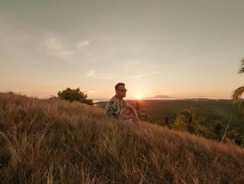 Man sitting on field against sky during sunset