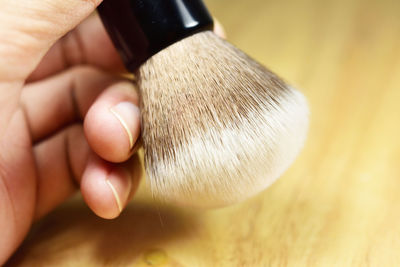 Cropped hand holding shaving brush on wooden table