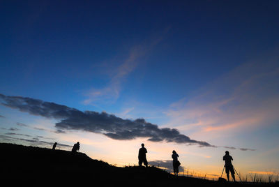 Silhouette people standing on landscape against sky during sunset