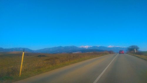 Empty road leading towards mountains against clear blue sky