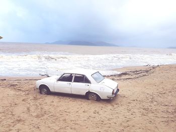 Vintage car wreck on beach against sky