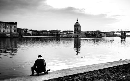 Rear view of man sitting on river in city against sky