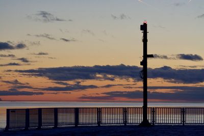 Silhouette wooden post by sea against sky during sunset