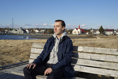 Man sitting on pier at beach against clear sky