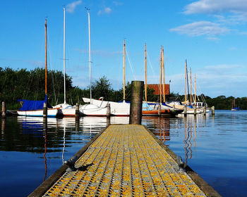 Sailboats moored in harbor at lake against sky