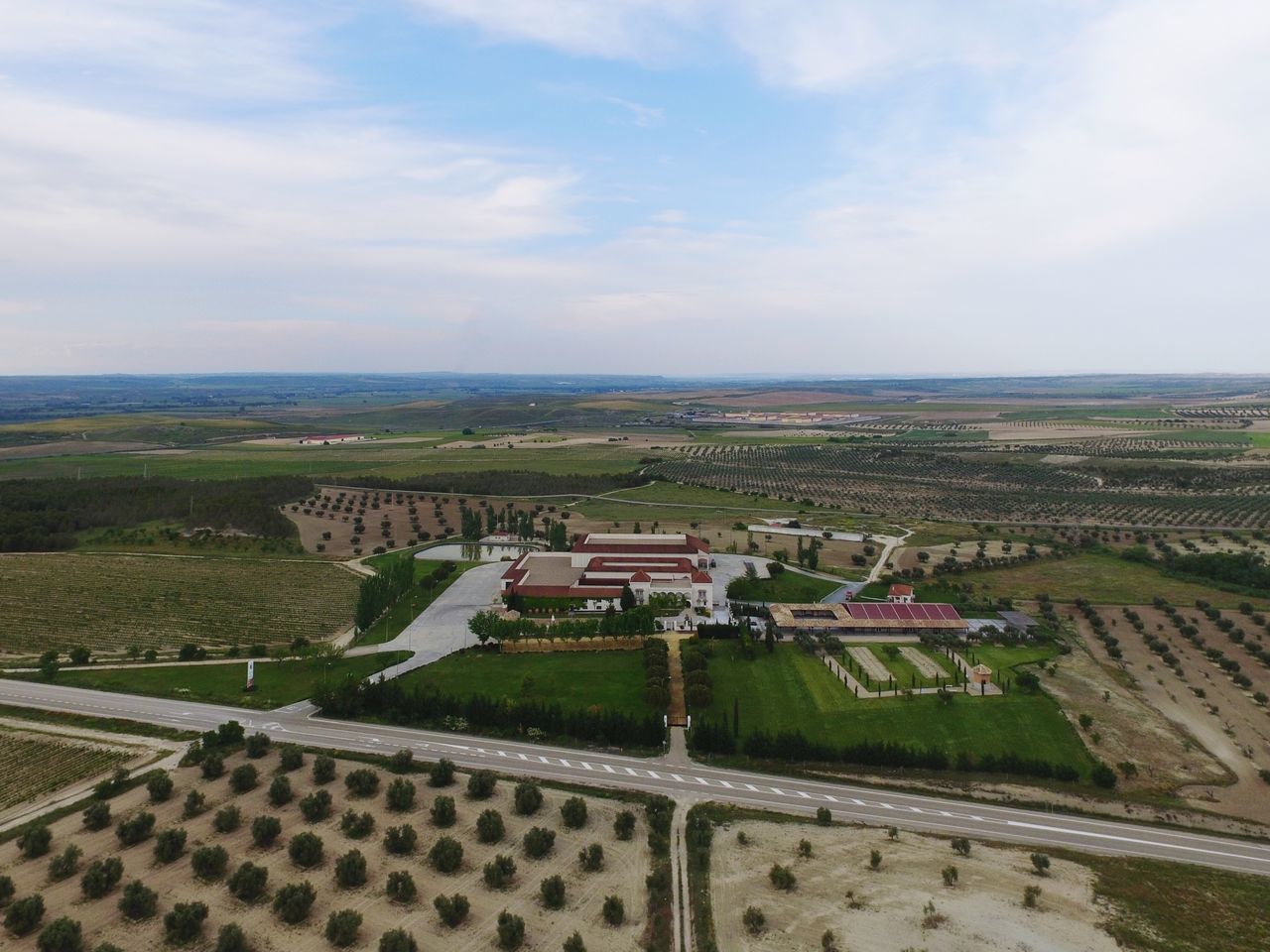 built structure, architecture, building exterior, sky, landscape, high angle view, agriculture, cloud - sky, rural scene, roof, farm, field, house, cloud, horizon over land, day, cityscape, cloudy, residential district, tree