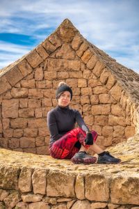 Man wearing hat sitting against brick wall