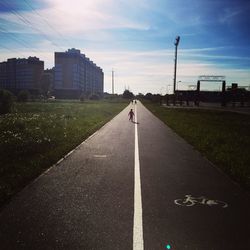 Rear view of woman walking on road in city against sky