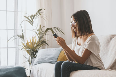 Woman using smart phone sitting on sofa at home