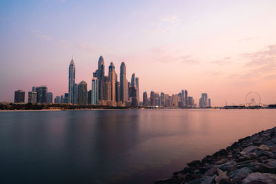 Sea by buildings against sky during sunset