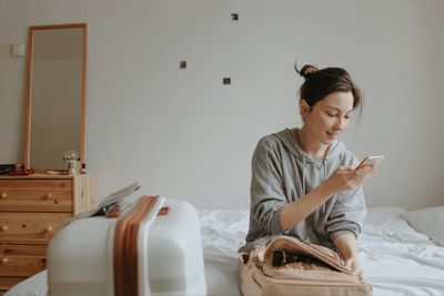 Woman with the baggage, smartphone and passport at home, preparing to flight