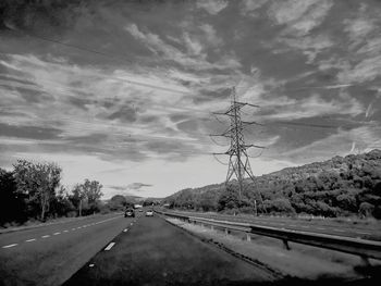 Road by electricity pylon against sky