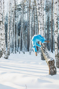 Rear view of mid adult man climbing tree in forest during winter