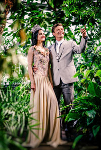 Smiling bride and groom standing amidst plants at botanical garden