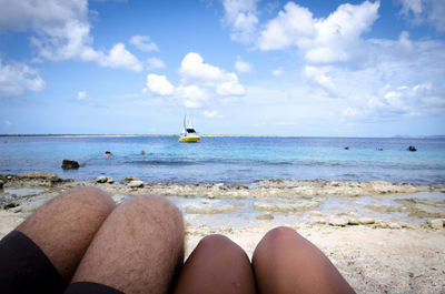 Low section of woman relaxing on beach against blue sky