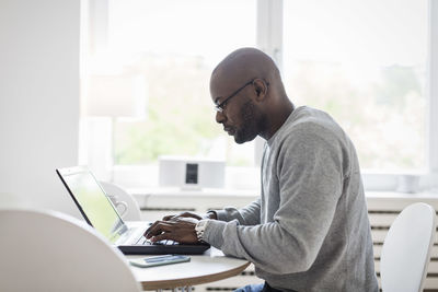 Side view of man using laptop at table in house