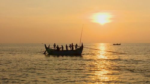 Silhouette people in boat sailing on sea against sky during sunset