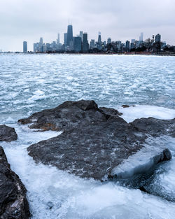 Scenic view of frozen sea by buildings against sky