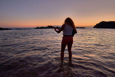 Rear view of woman standing on beach during sunset