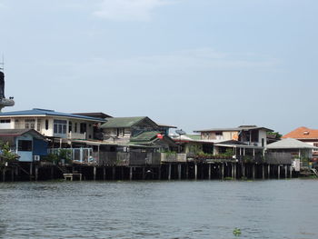 Houses by river against buildings in city against sky