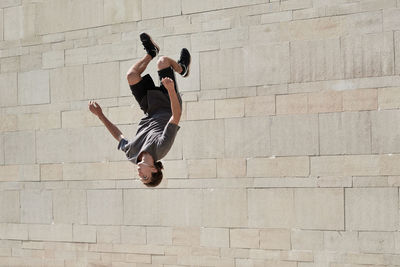 Upside down of young male doing somersault while practicing parkour in urban area in summer