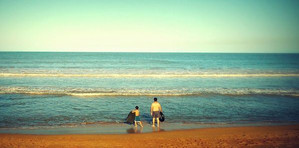 Rear view of men walking on beach against clear sky