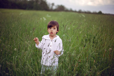 Boy child in a green field in summer in a white shirt with a hood made  linen in shorts and sandals