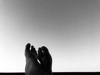 Low section of man with feet up against clear sky