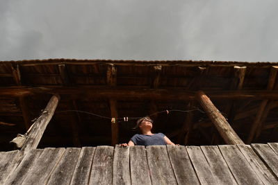 Boy sitting on wood against sky