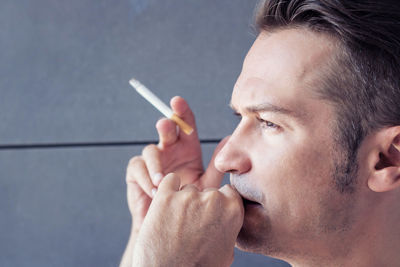 Close-up of thoughtful man smoking cigarette against wall