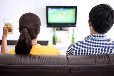 Rear view of men and women watching soccer on sofa