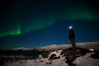 Rear view of person standing on snow against sky at night