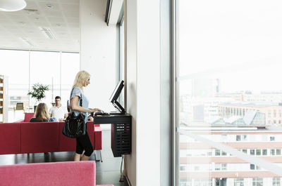 Female student using desktop pc at university library while friends studying in background