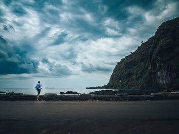 Rear view of man standing on beach against blue sky and mountain. moroni, comoros island.