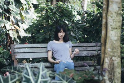 Smiling young woman sitting on bench against trees