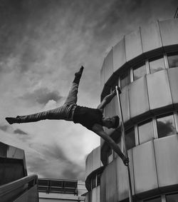 Low angle view of man exercising against buildings and sky