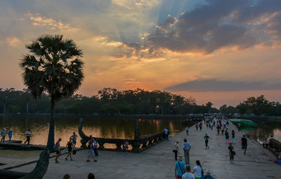 People by palm trees against sky during sunset