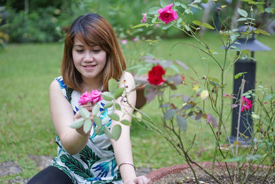 Young woman touching pink rose while crouching at park