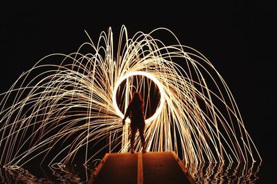 Silhouette woman standing by illuminated ferris wheel against sky at night