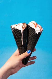 Hand holding ice cream against blue sky