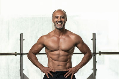 Portrait of shirtless man with hand on hip standing in gym