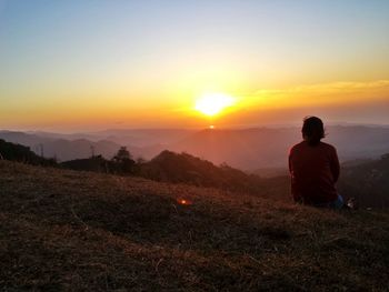 Rear view of woman sitting on mountain during sunset