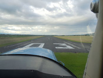 Road passing through field against cloudy sky