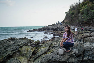 Young woman on rock by sea against sky